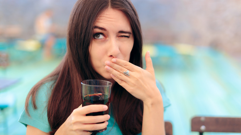 Woman covering her mouth, with a glass in her hand