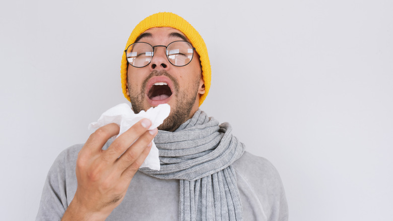 Man with yellow hat sneezing