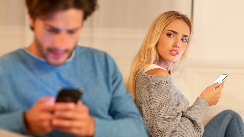 Woman looking over her shoulder suspiciously at a man texting