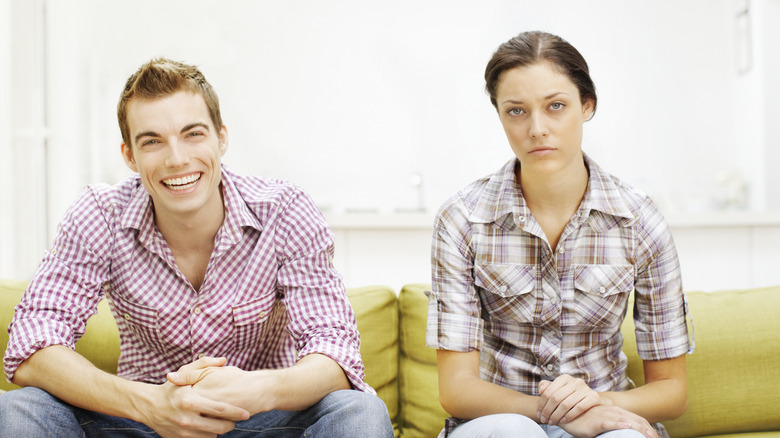 Two people sitting on couch. One is happy and the other is sad