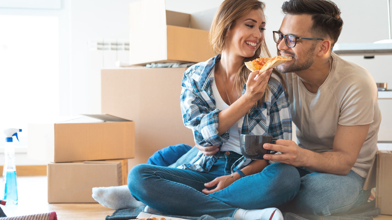 Couple eating pizza while sitting in front of moving boxes