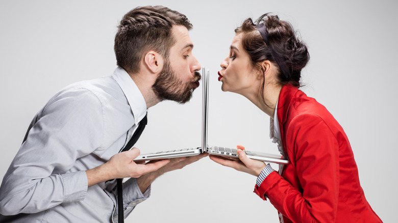 young businessman and businesswoman with laptops kissing screens