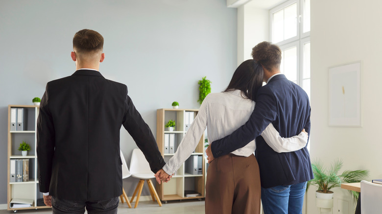 A woman is hugging a man and holding another man's hand
