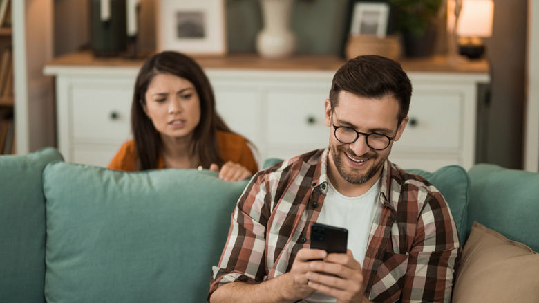A man is using his mobile phone while a concerned woman watches