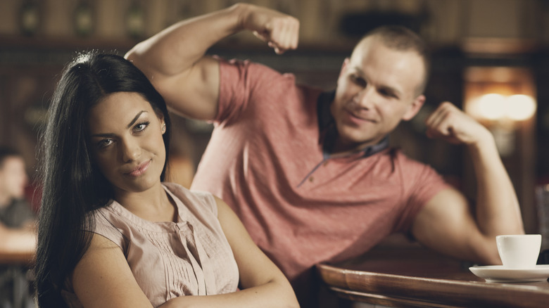 Young woman is unimpressed with a flexing man