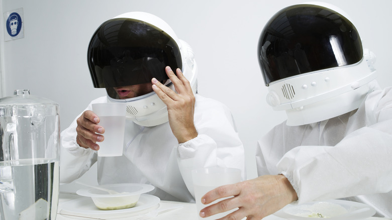 People sitting at a table for a meal wearing mock space suits