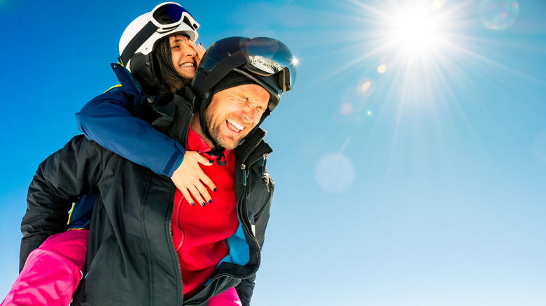 Couple laughing and squinting against the sun on the ski slopes