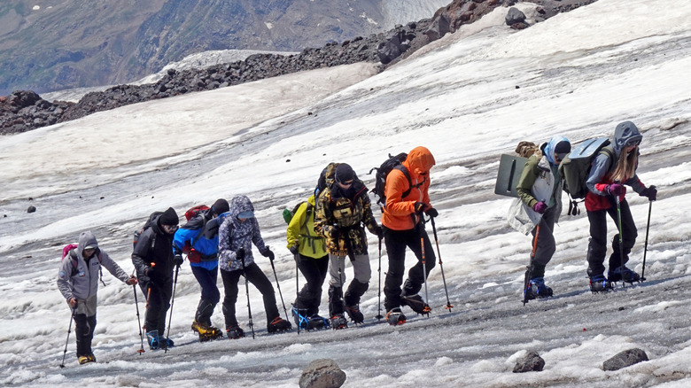 Nine people in heavy mountaineering gear climbing up icy Everest path