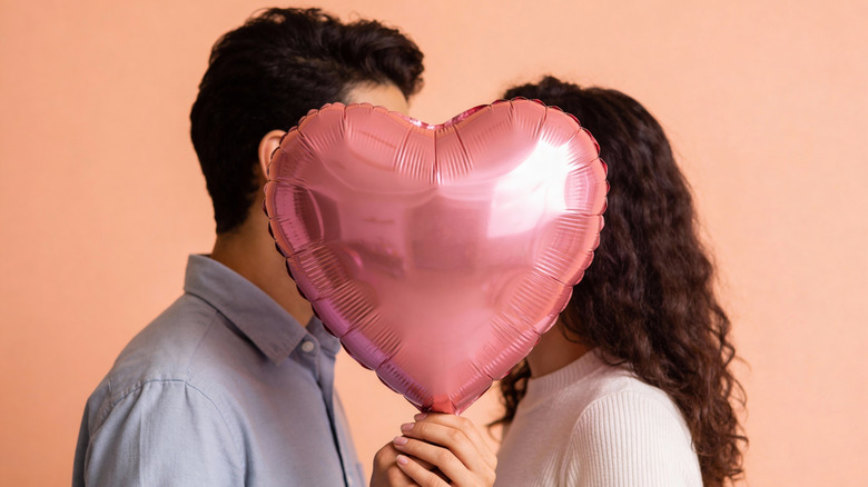 A couple's faces covered with a pink balloon