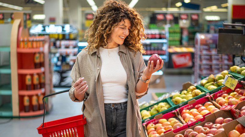 Woman holding a red apple and red shopping basket