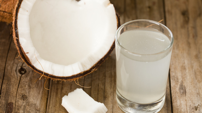 A glass of coconut water on table next to a halved coconut fruit
