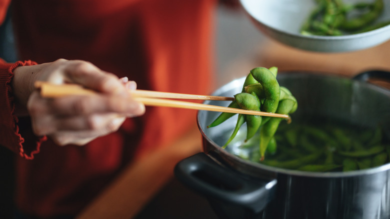 Hand straining cooked edamame from pot of water and placing it in a bowl