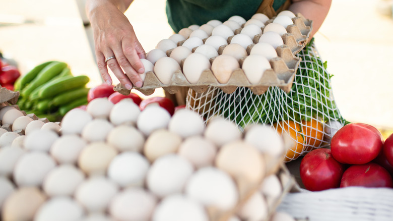 Person gathering eggs next to vegetables at a farmer's market