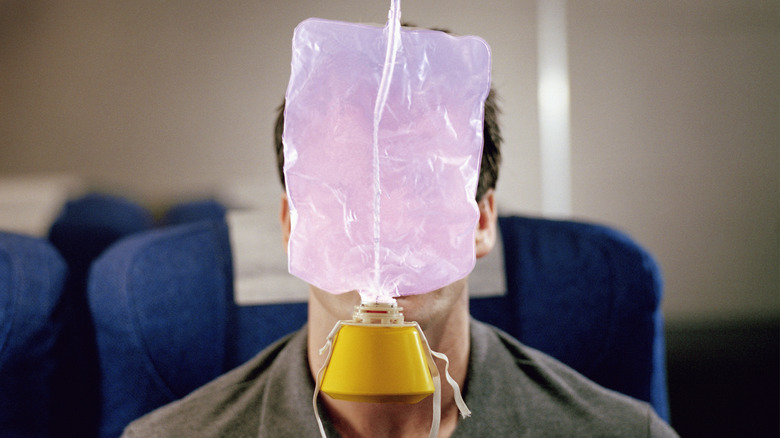An oxygen mask hangs from the ceiling of a plane cabin in front of a passenger