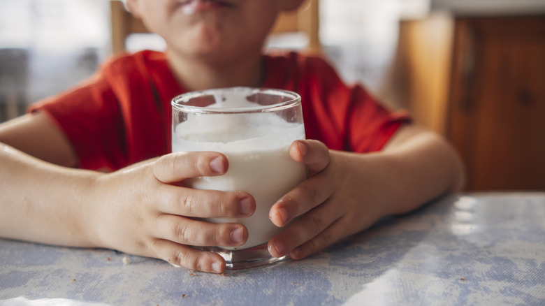 child's hands holding glass of milk