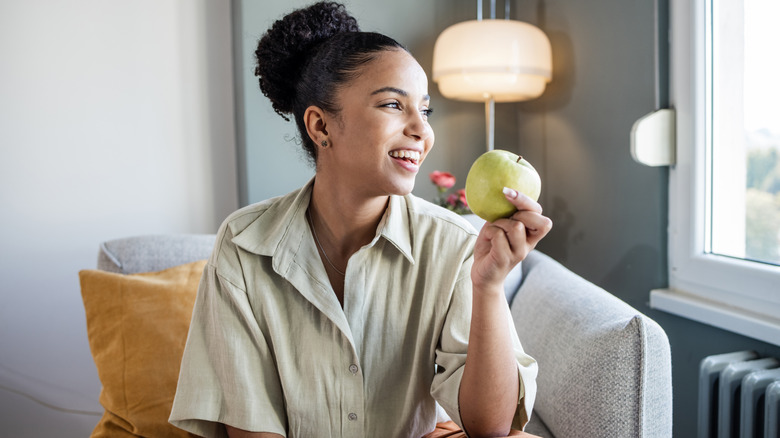 Woman holding green apple while sitting on couch