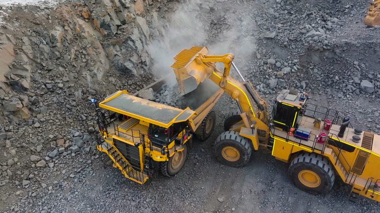 Heavy machinery dumping rock into a dump truck in an open mine