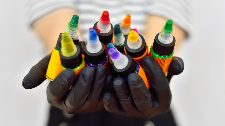 Gloved hands holding different bottles of tattoo ink colors