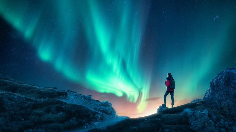 Silhouette of a backpacker standing on a hill or mountain top under the aurora borealis