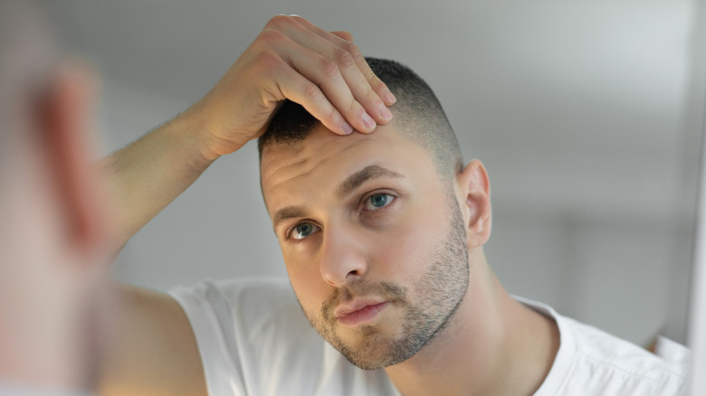 Young man examining skin and hair in the mirror
