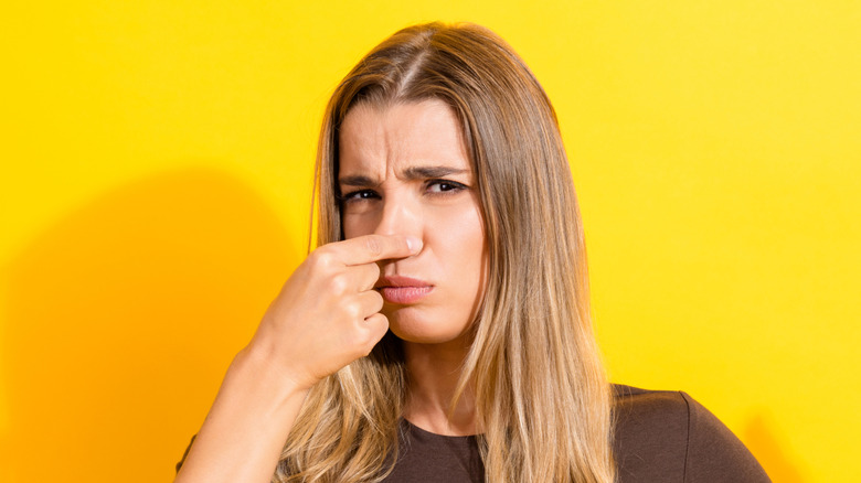 A woman is holding her nose against a yellow background