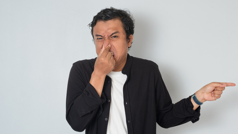 A man is holding his nose and pointing with a finger