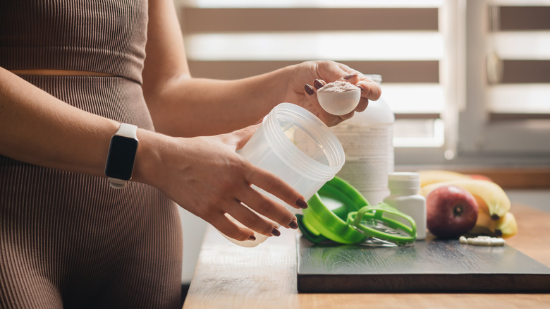 A person in athletic clothes scoops powder into a cup.