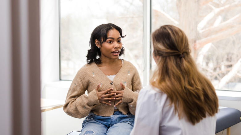 Young woman sits in doctors office and talks to her female doctor