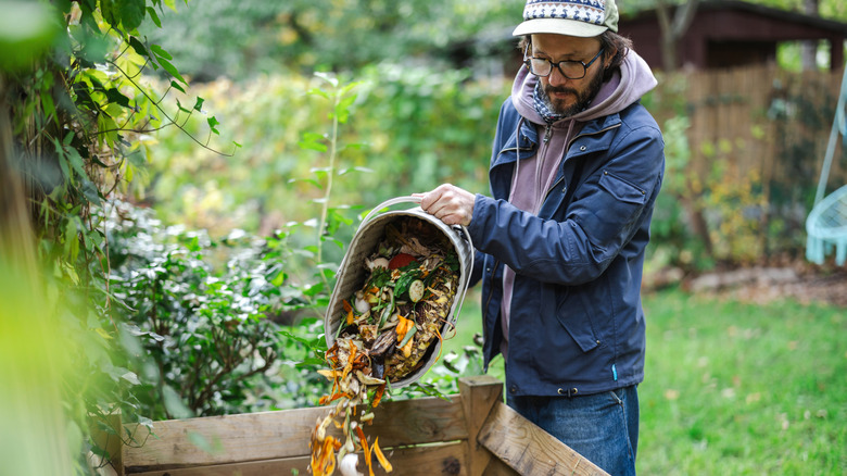 A man throwing vegetable scraps into a compost container in a backyard