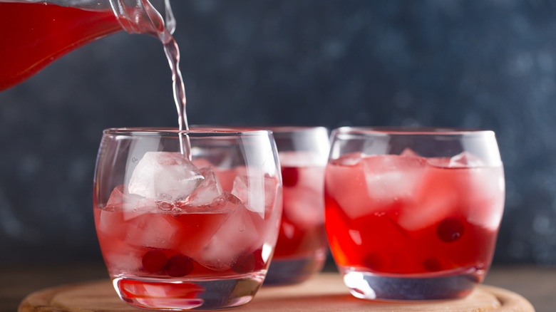 Pouring a glass of cranberry juice over ice cubes