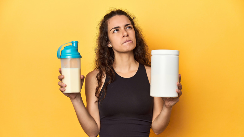Woman holding up a prepared shake and protein powder mix
