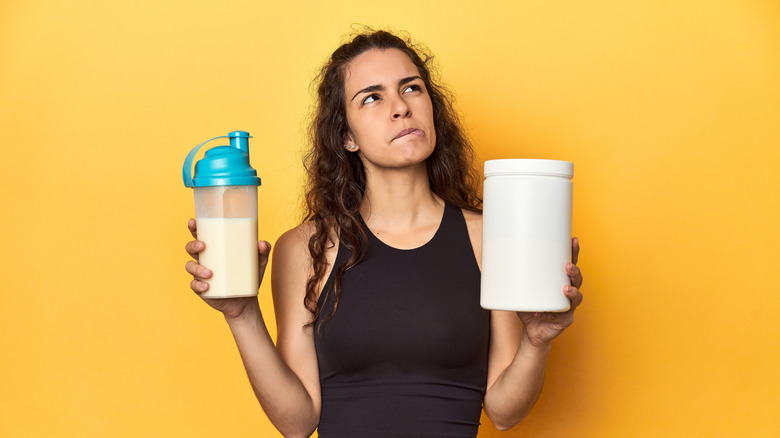 Woman holding up a prepared shake and protein powder mix