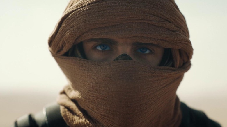 Paul Atreides wearing stillsuit and looking at camera with blue eyes
