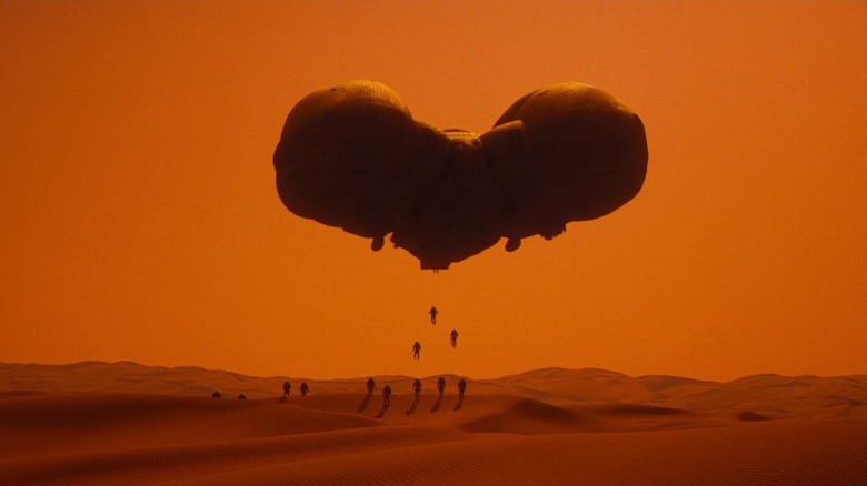 Aircraft floating over dunes as soldiers drop to surface