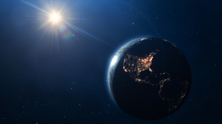 Earth in space in the foreground with the sun glinting in the background