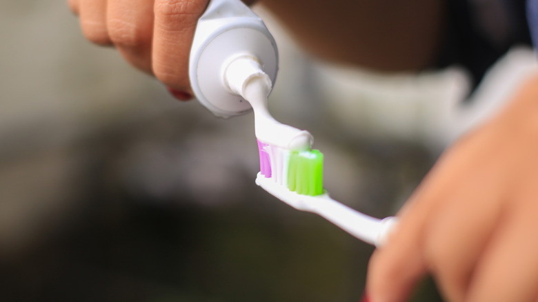 Person putting toothpaste on a toothbrush with pink, white, and green bristles