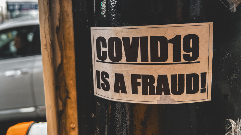 An anti-vaccine poster on a street pole reading "COVID19 IS A FRAUD!" against an overcast urban backdrop in Vancouver, Canada