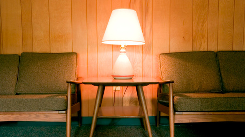Retro style living room with a lamp on a table, two couches, and wood paneling on the walls