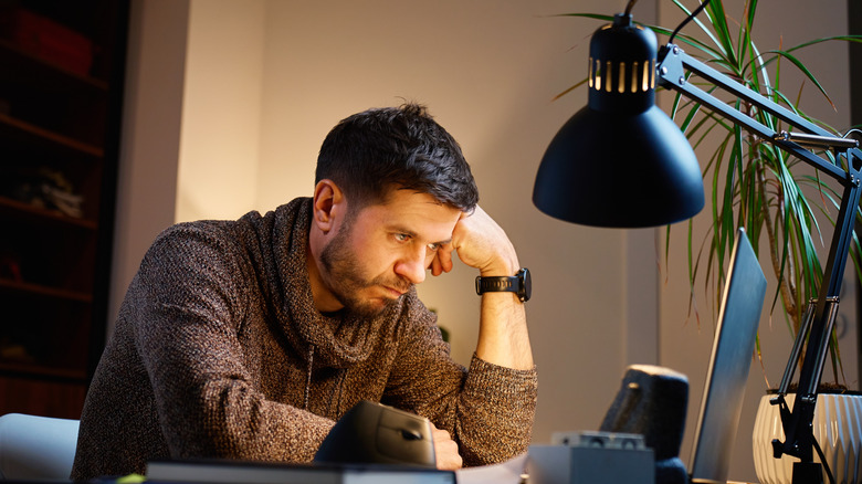 Man wearing a sweater sitting at a desk, doing focused work on a computer
