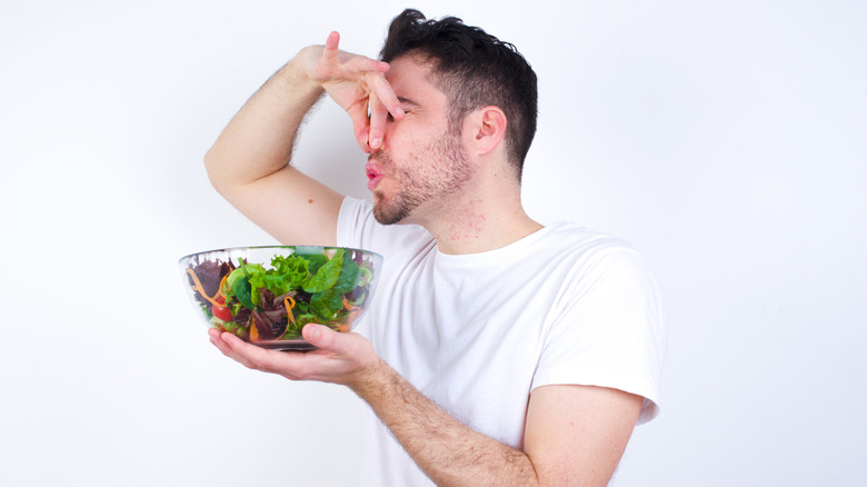 Man holding his nose with one hand and a salad bowl with the other
