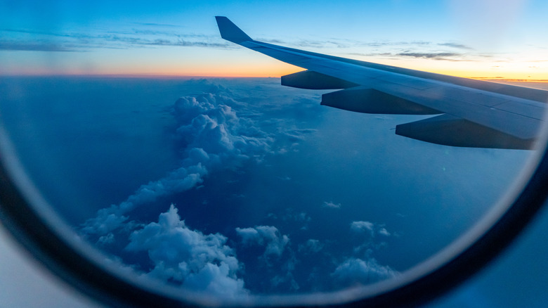 A view of the clouds, horizon, and plane wing from a window seat during a flight