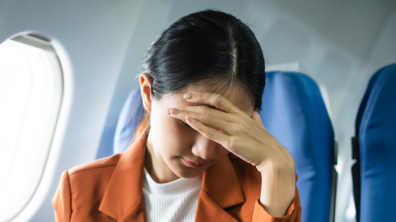 A plane passenger with her head down and her hand hiding her face in embarrassment
