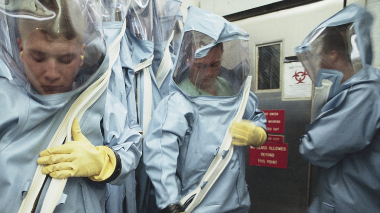 Soldiers at Fort Detrick zipping on full-body hazmat suits in a containment room