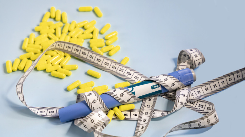 Ozempic syringe pen and measuring tape with a bunch of yellow pills in the background