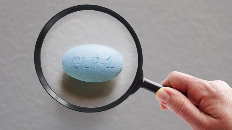 A hand holding a magnifying glass over a GLP-1 pill
