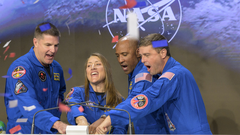 The crew members from the Artemis II mission press a button together while confetti falls around them.