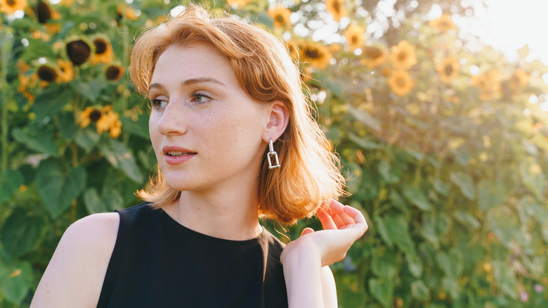 A redheaded woman looking to the side in front of sunflowers.