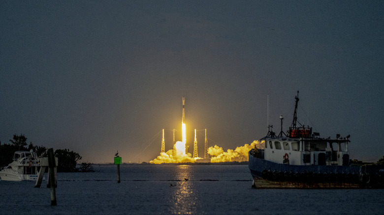 A SpaceX Falcon 9 rocket launches, clearing the lightning arrestor towers at dusk