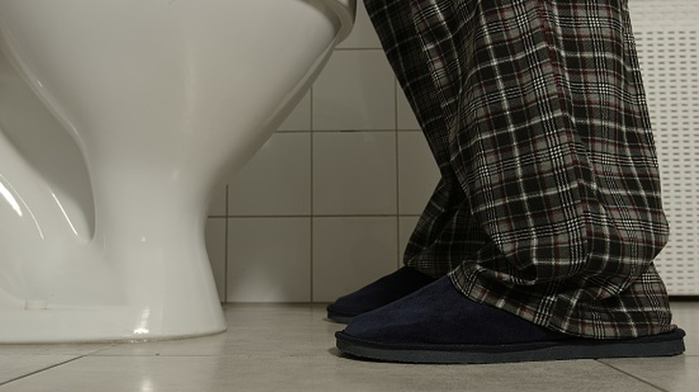 View of toilet from the floor with person in pajama pants and slippers standing in front of it
