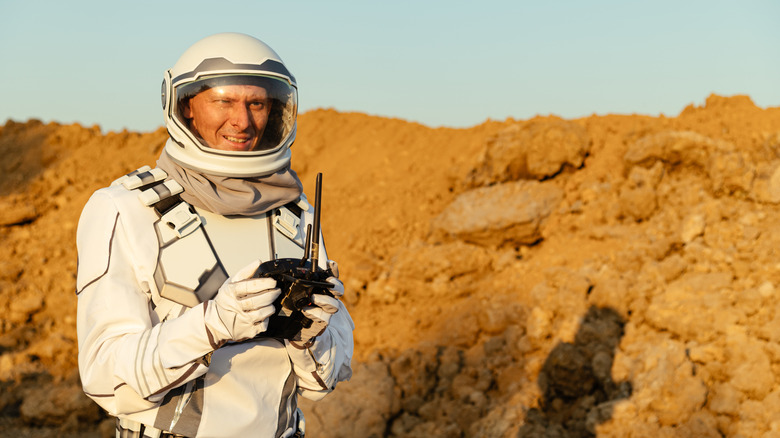 Astronaut in space suit holding equipment standing in front of rocks